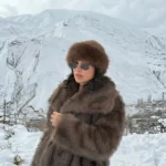 استایل مدل زنانه با کلاه روسی دورخز قهوه‌ای و پالتو خزدار در منظره برفی